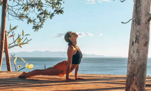 woman doing yoga, updog, on studio deck with ocean in background