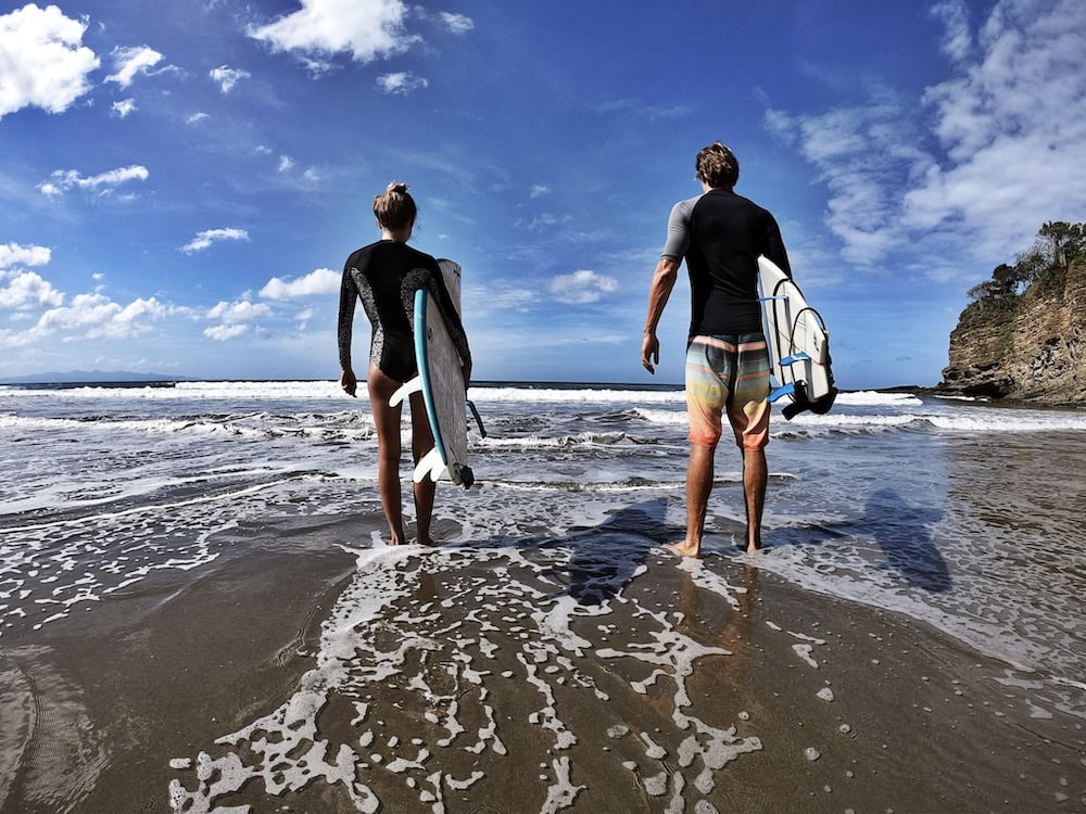 Man and woman walking into the water with their surfboards